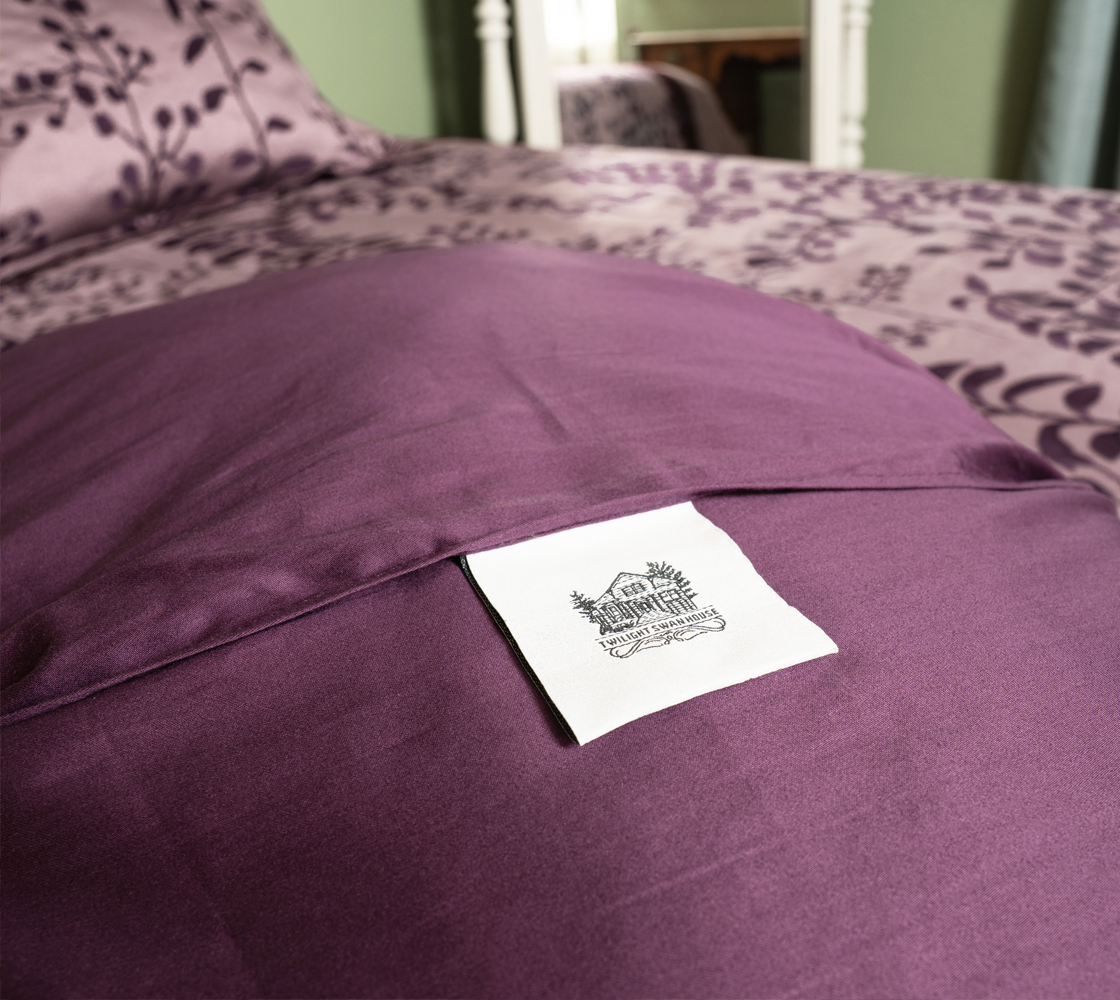 Close-up of a purple pillow with a brand label on a bed with matching bedding.