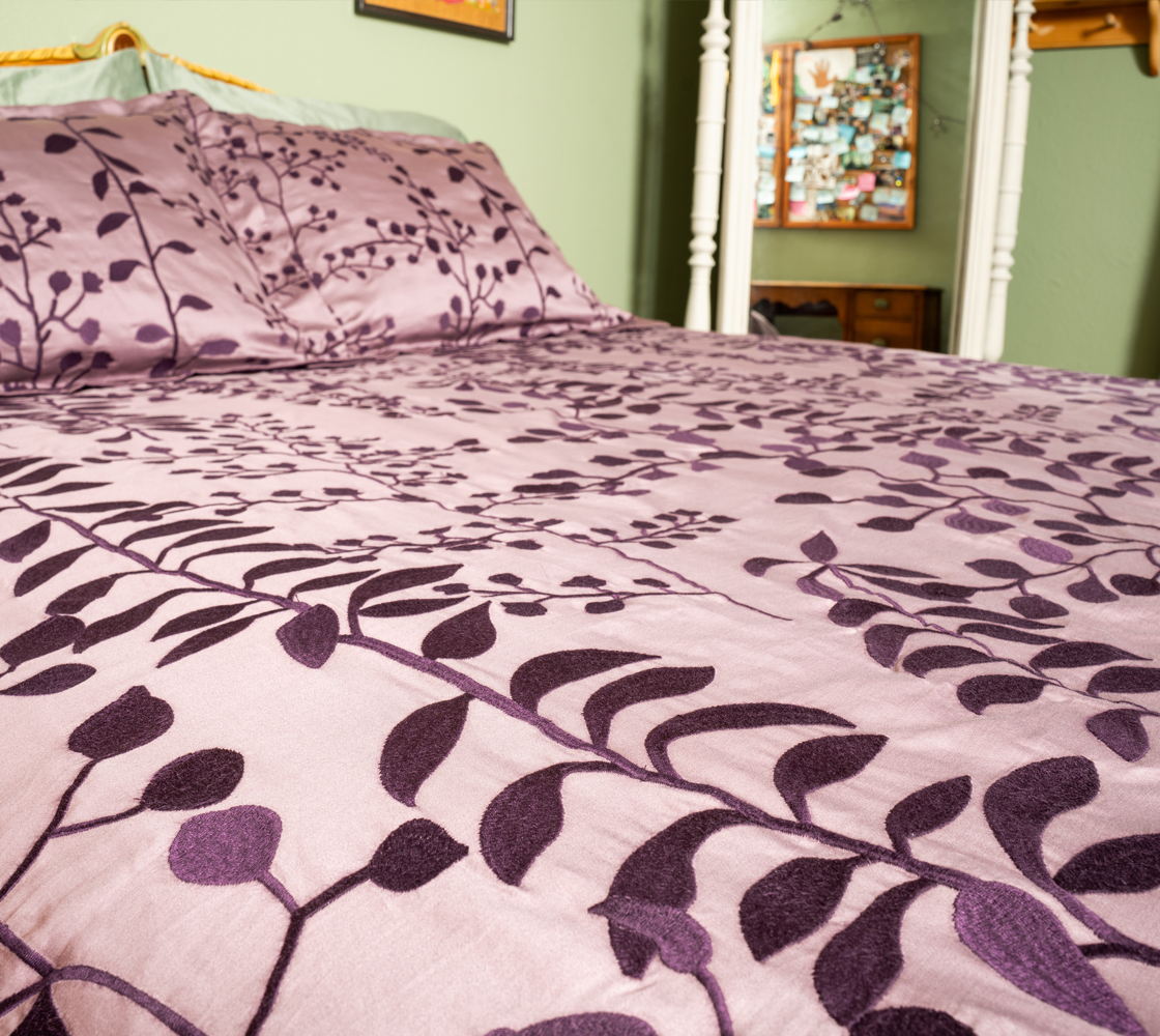 Bed with purple floral bedding in a room with green walls and a dresser.